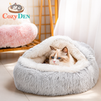 Cat lying in a fluffy gray pet bed with 'Cozy Den' branding.