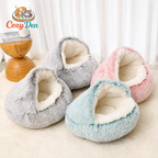 Four Cozy Den pet beds in light gray, mint blue, and pastel pink, arranged on a beige floor in front of white curtains. A wooden bowl and a Cozy Den logo are visible in the background.