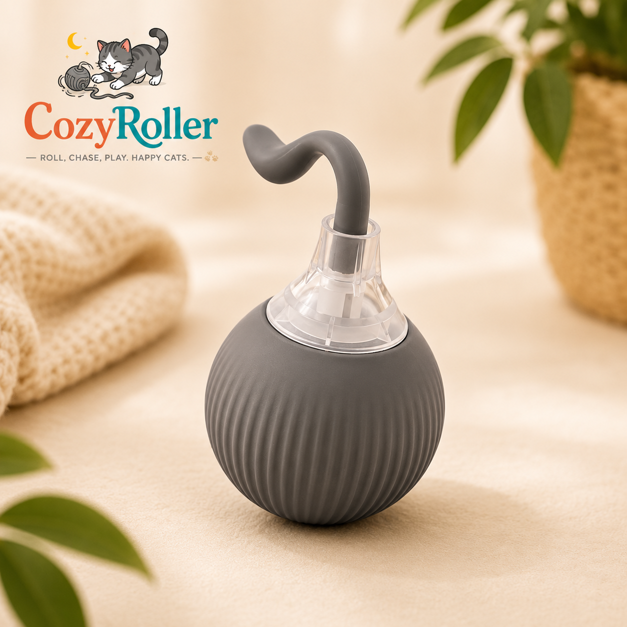 A CozyRoller pet toy shaped like a small rounded gray container with a curved gray handle and a clear top, shown on a warm beige surface with soft background props including a knit blanket, plant leaves, and a basket. CozyRoller logo appears in the upper left.